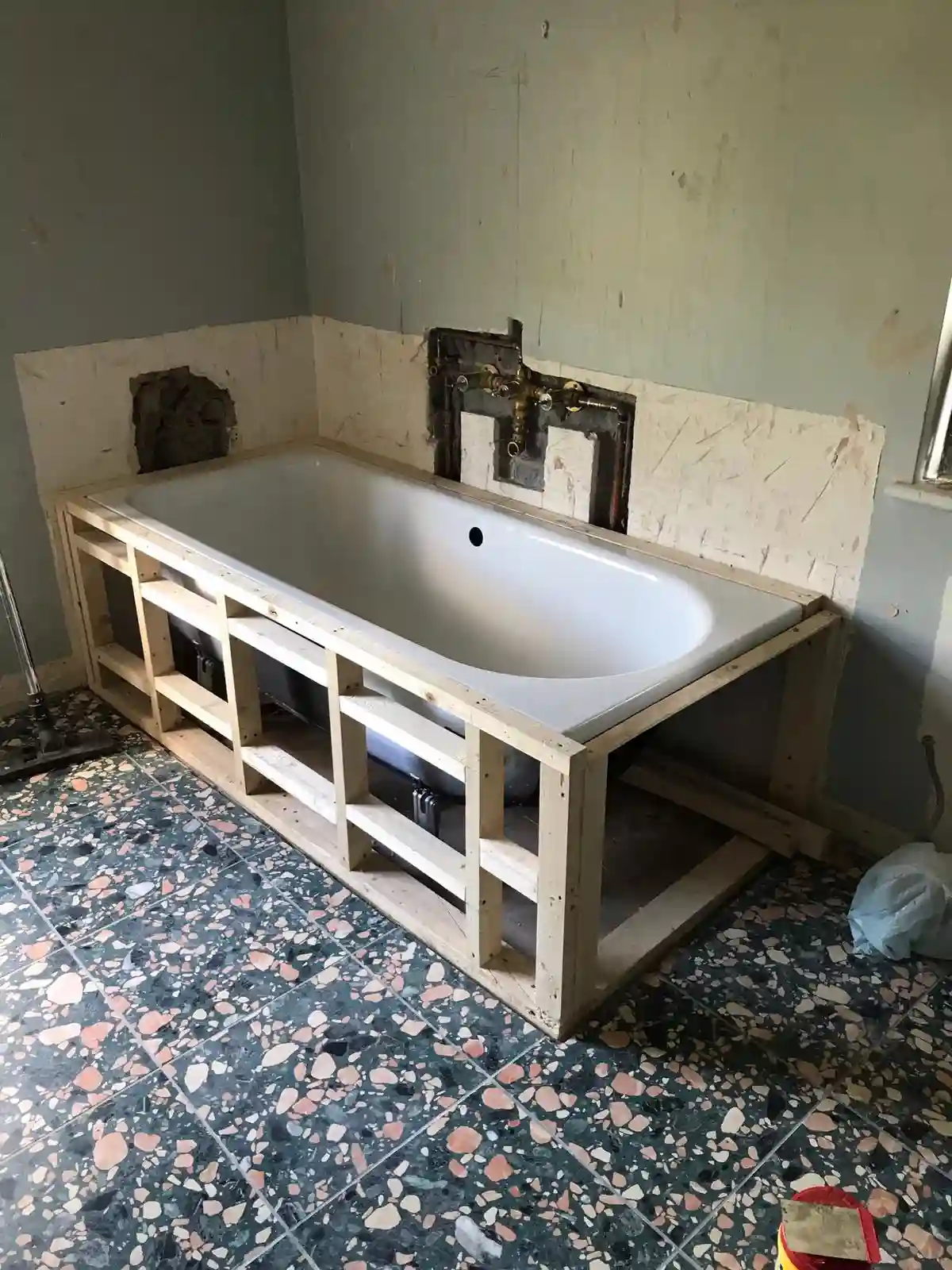 Bath installation in progress with exposed plumbing connections and timber support frame