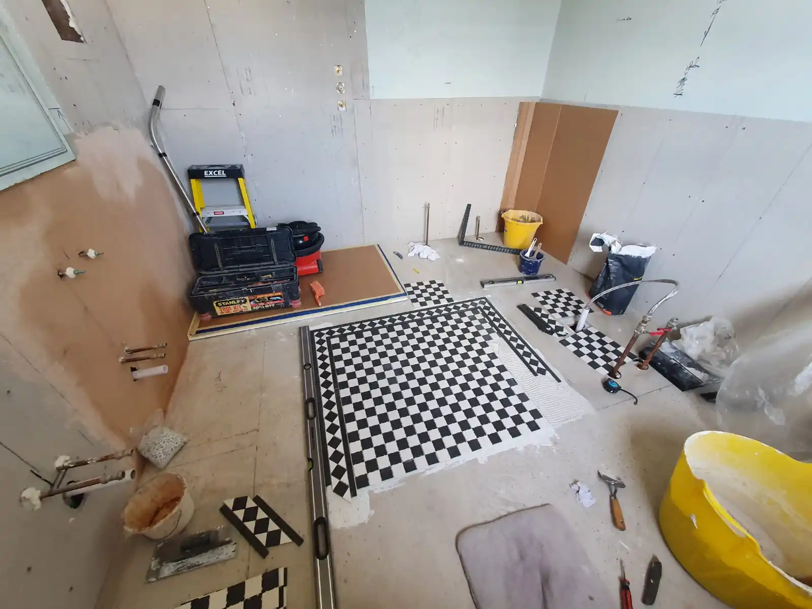 Bathroom installation in progress with new flooring and exposed plumbing pipework