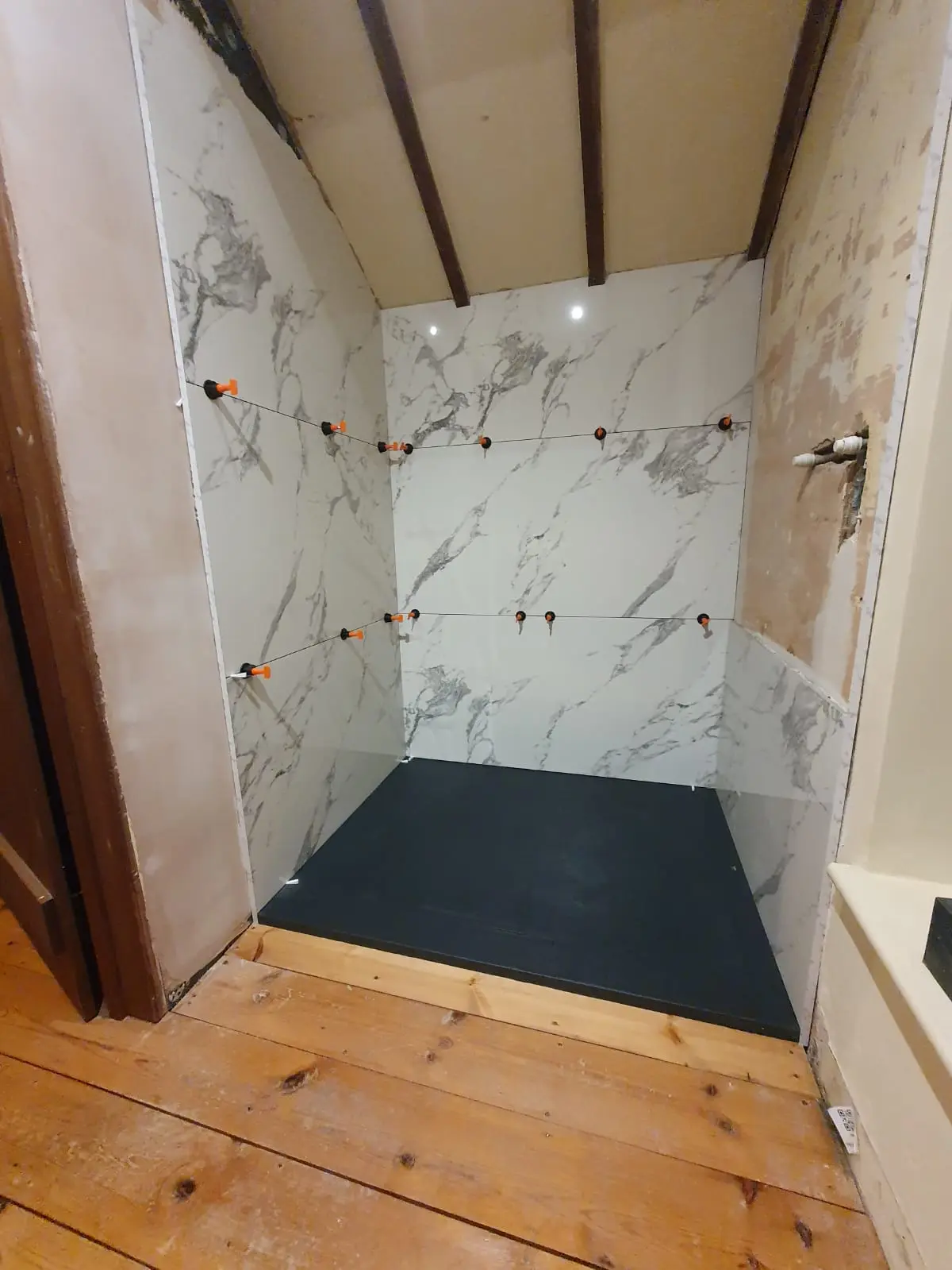 Bathroom shower installation in progress with tiled walls, shower tray and exposed plumbing connections