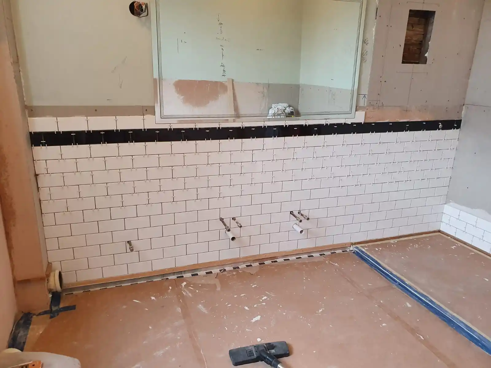 Bathroom plumbing installation in progress with wall tiling and exposed pipe connections