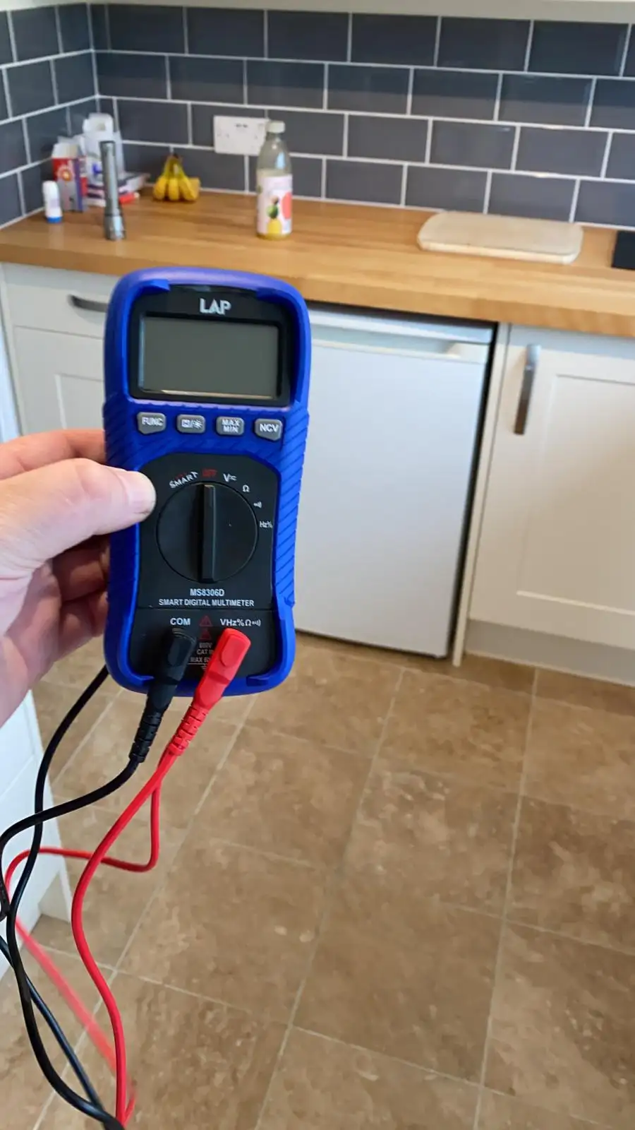 Electrician using a digital multimeter to test an electrical circuit in a kitchen