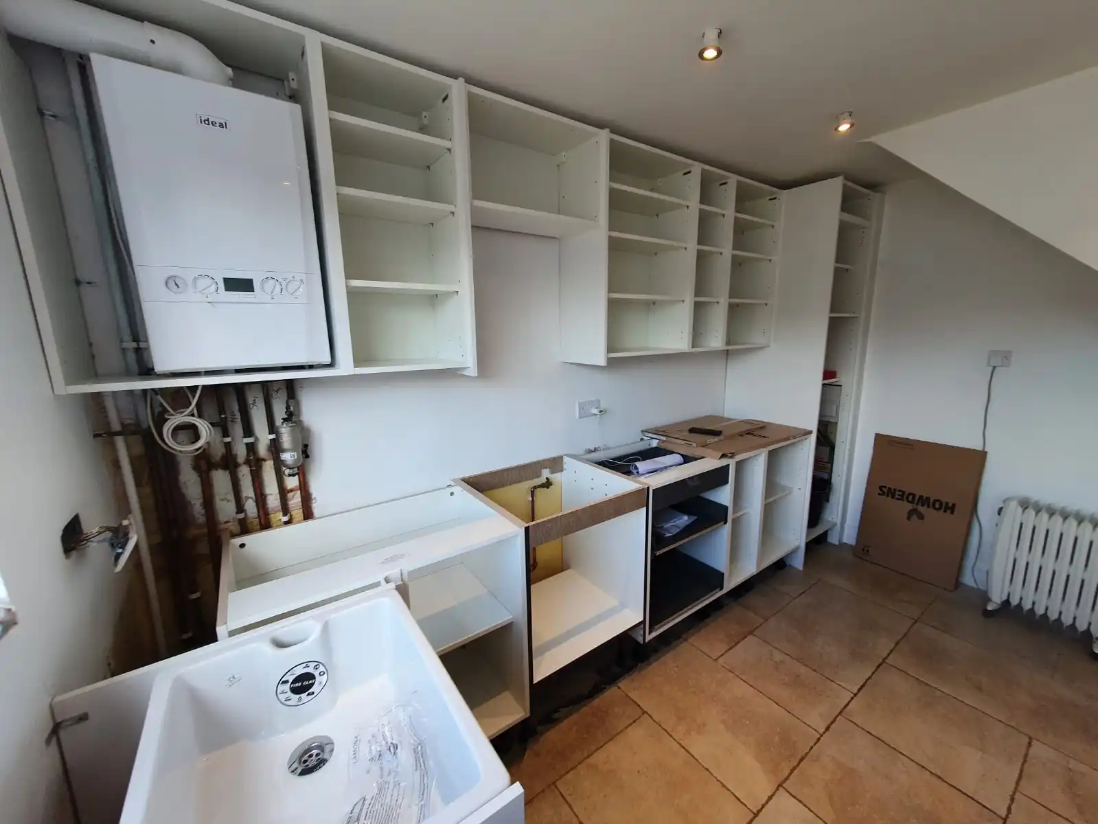 Boiler installation and kitchen plumbing with wall-mounted boiler, sink and exposed pipework
